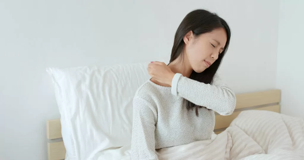 Woman feeling shoulder pain on bed